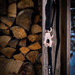 Black PVC dog leash with rose gold hardware, hanging from a wooden post with a stacked woodpile in the background.