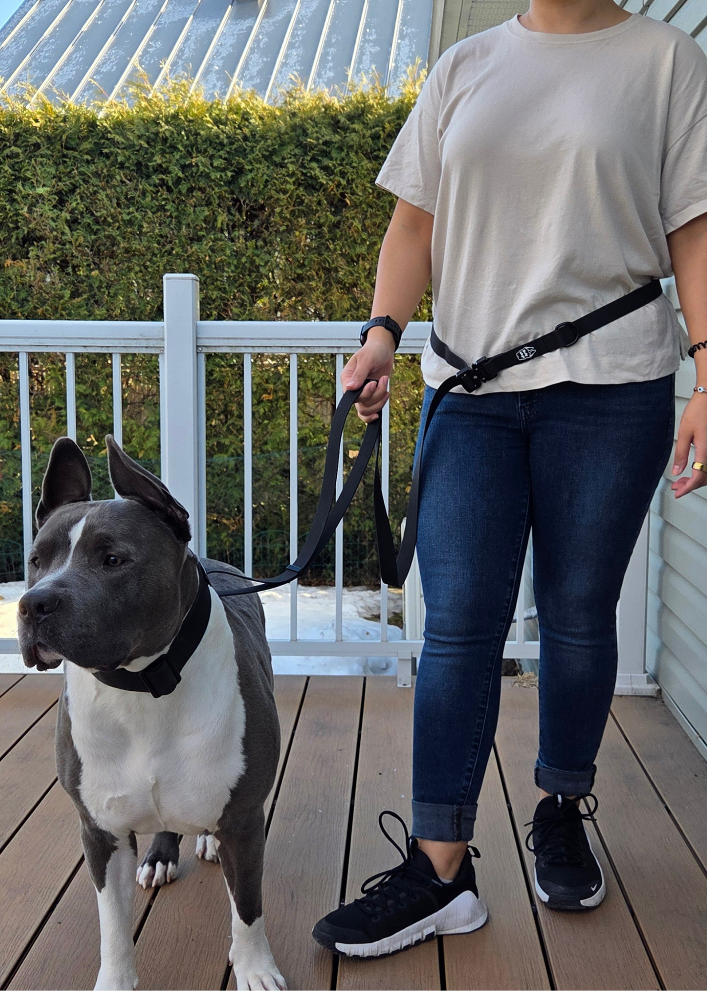 Person walking a dog using a multi-way hands-free dog leash on a wooden deck.