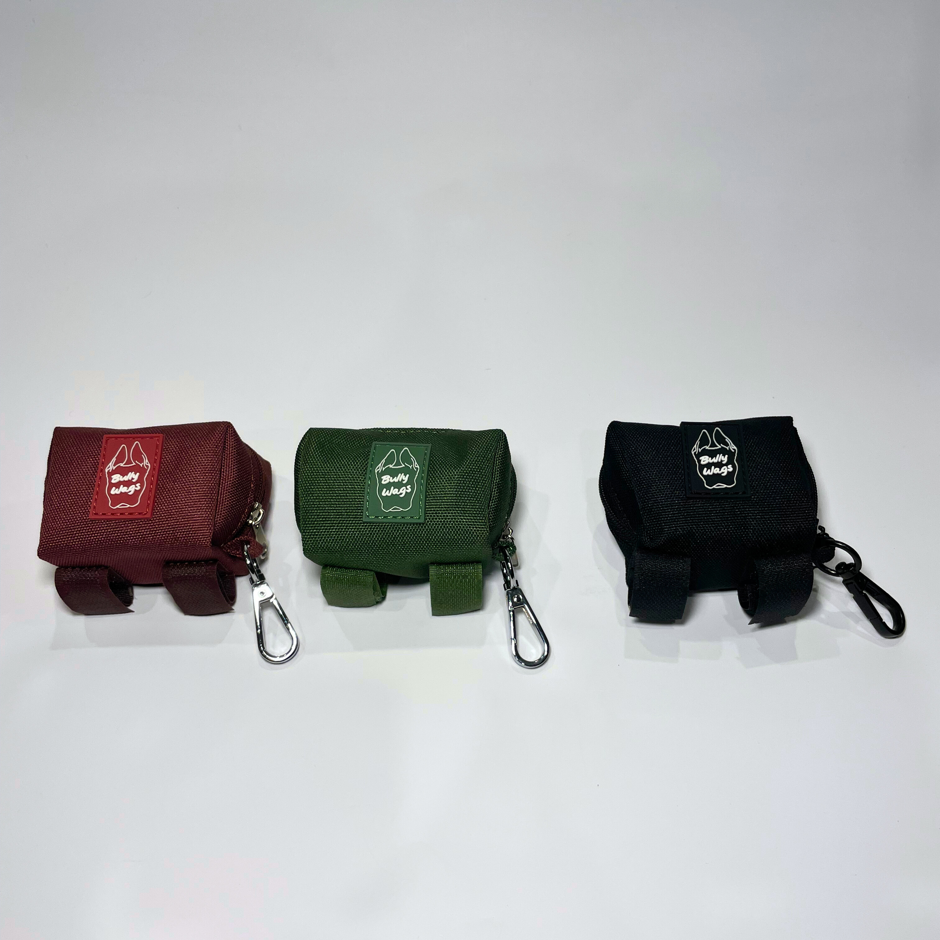 Three portable poop bag dispensers in cherry wine, cactus green, and black attached to matching leashes, displayed on a white background.