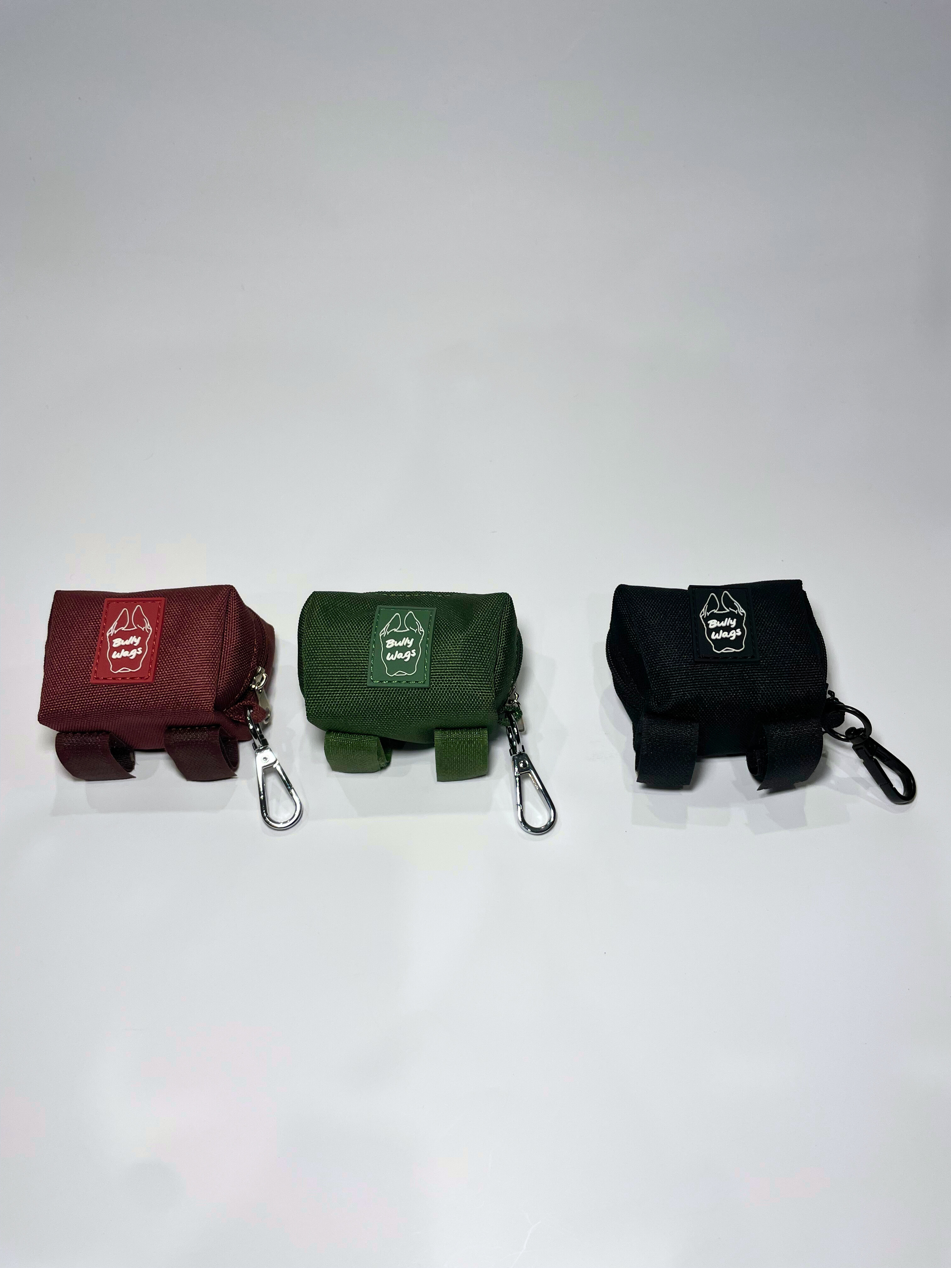 Three portable poop bag dispensers in cherry wine, cactus green, and black attached to matching leashes, displayed on a white background.